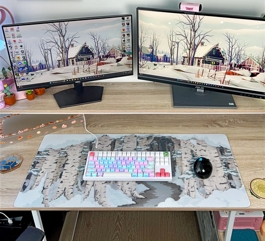 Two computer monitors on a desk with a keyboard and mouse, featuring a winter-themed birch forest landscape desk mat
