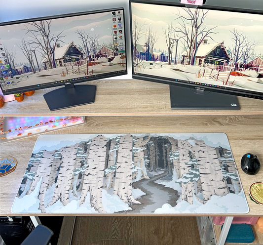 Two computer monitors on a desk with a large mouse pad desk mat featuring a winter birch forest landscape design.