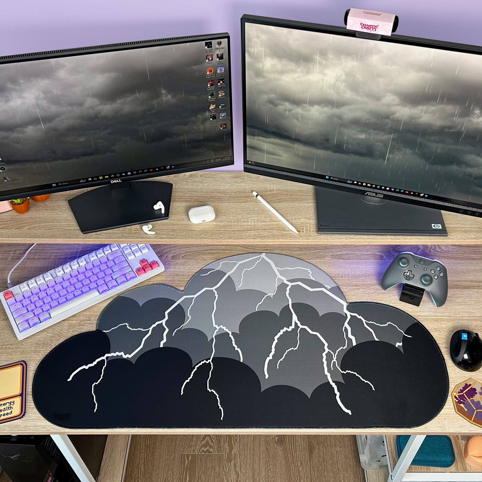 Computer setup with dual monitors, keyboard, mouse, gaming controller, and black to grey ombre with lightning cloud shaped desk mat on a desk.