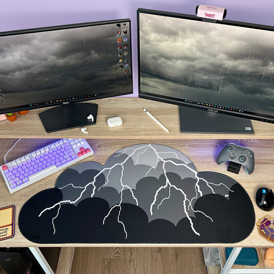 Computer setup with dual monitors, keyboard, mouse, gaming controller, and black to grey ombre with lightning cloud shaped desk mat on a desk.