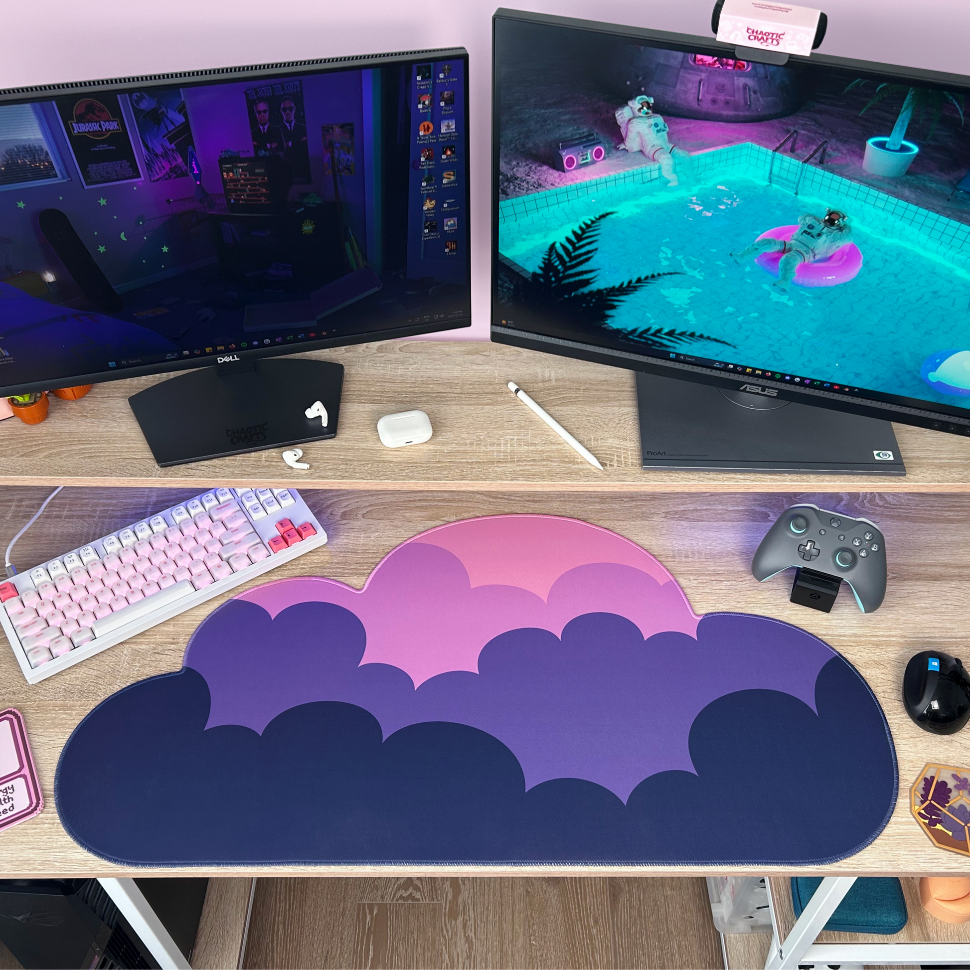 Gaming setup with two monitors, keyboard, mouse, gaming controller and dark purple pink ombre cloud shaped desk mat on a desk.